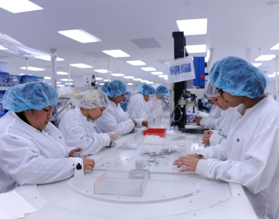 Providien Medical Device Assembly. Lab technicians wearing white coats and blue hair covers assembling medical devices.